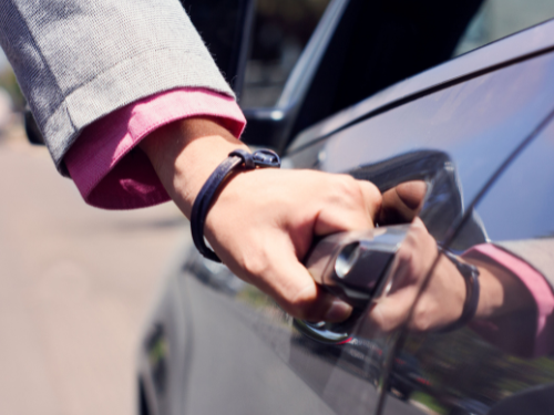 Eine Hand greift nach dem Türgriff eines Autos.