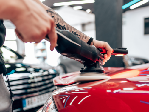 Hände polieren die Motorhaube eines roten Autos mit einer Schleifmaschine.