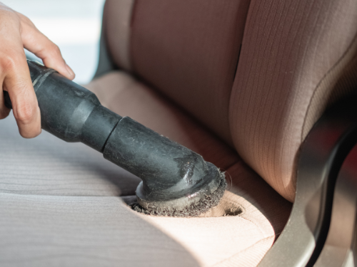 Hand mit einem Staubsauger, der einen Autositz reinigt.