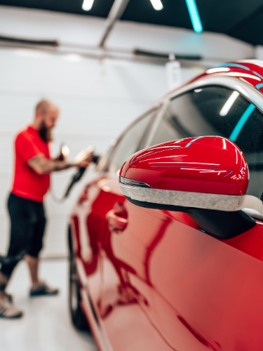 Roter Autoaußenspiegel mit einer Person im Hintergrund, die daran arbeitet.