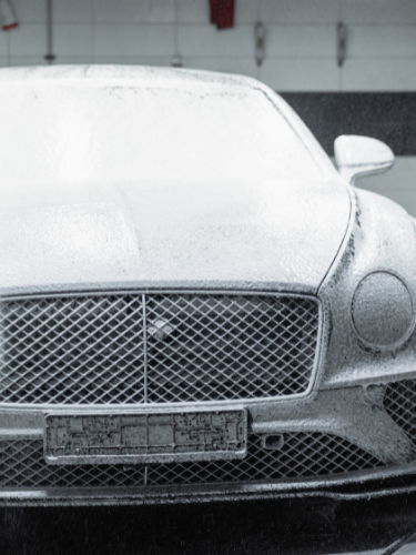 Ein schneeweißer Bentley, bedeckt mit Schaum, in einer Waschstraße.