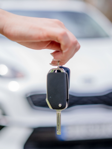 Eine Hand hält einen Autoschlüssel vor einem weißen Auto.