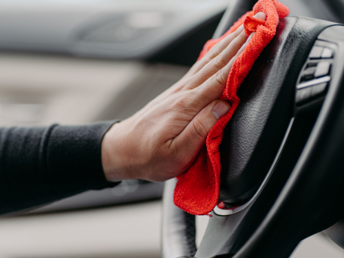 Eine Hand reinigt das Lenkrad eines Autos mit einem roten Tuch.